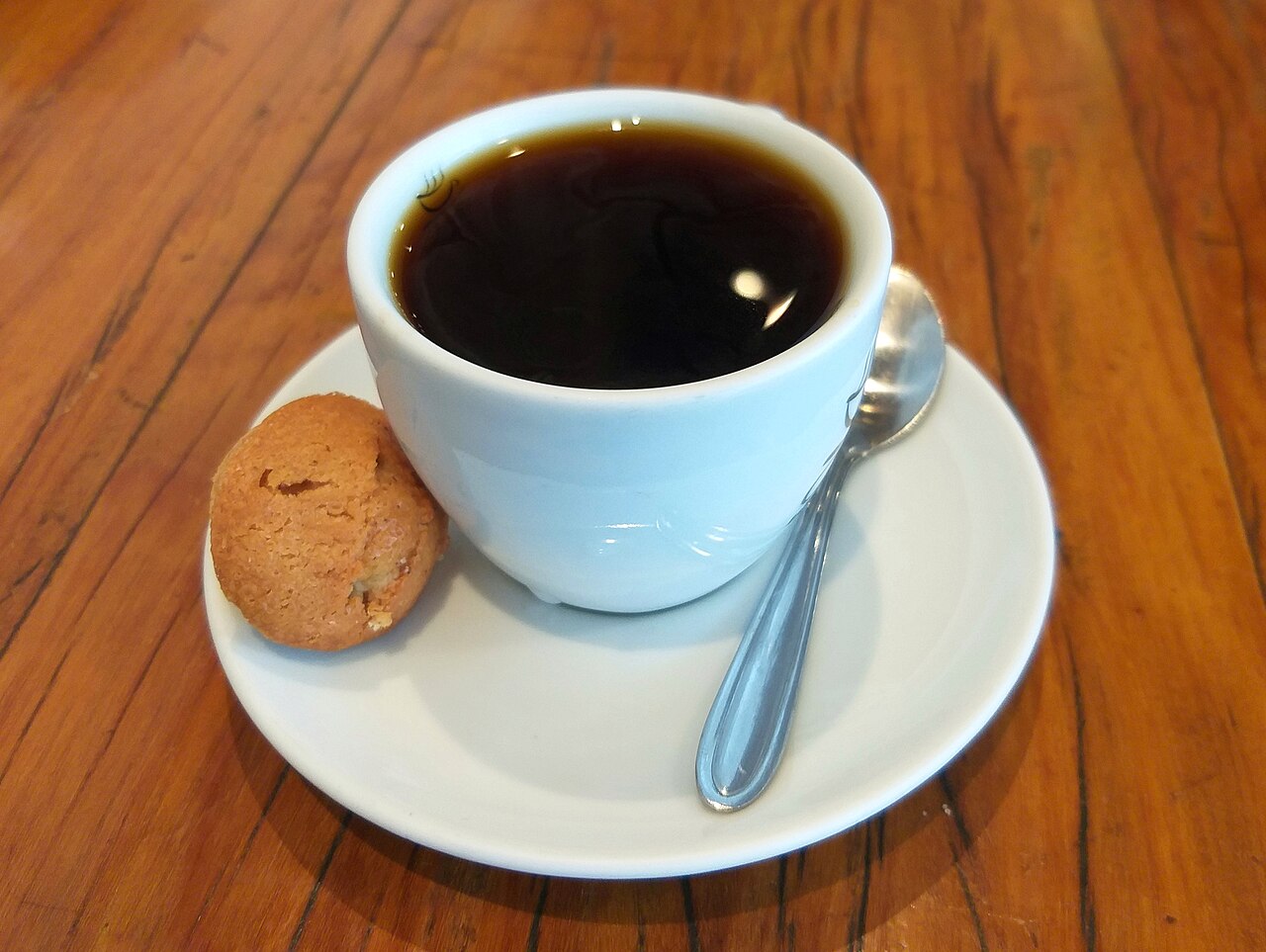 A close-up shot of a barista performing a pour-over coffee, with water pouring from a gooseneck kettle into a V60 dripper over a ceramic mug.